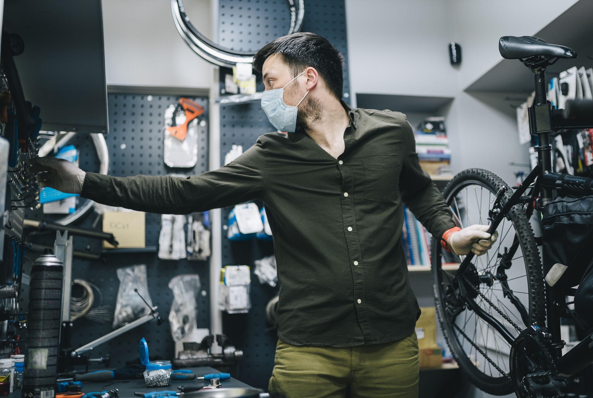 Mechaniker repariert Fahrrad in der Werkstatt tragen covid 19 Maske. Arbeiter des Fahrradladens fixiert Fahrrad während Coronavirus Quarantäne in Schutzmaske. Wartungszyklus des Reparaturarbeiters. Sportshop-Konzept