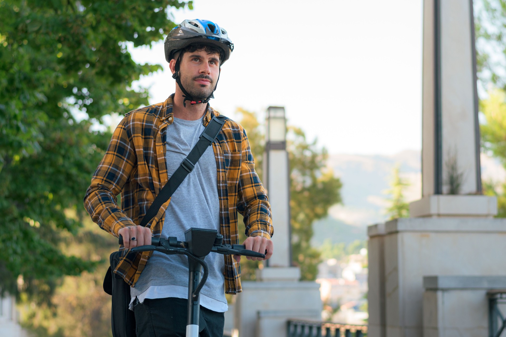 Porträt eines jungen Mannes, der einen Elektroroller mit Helm fährt