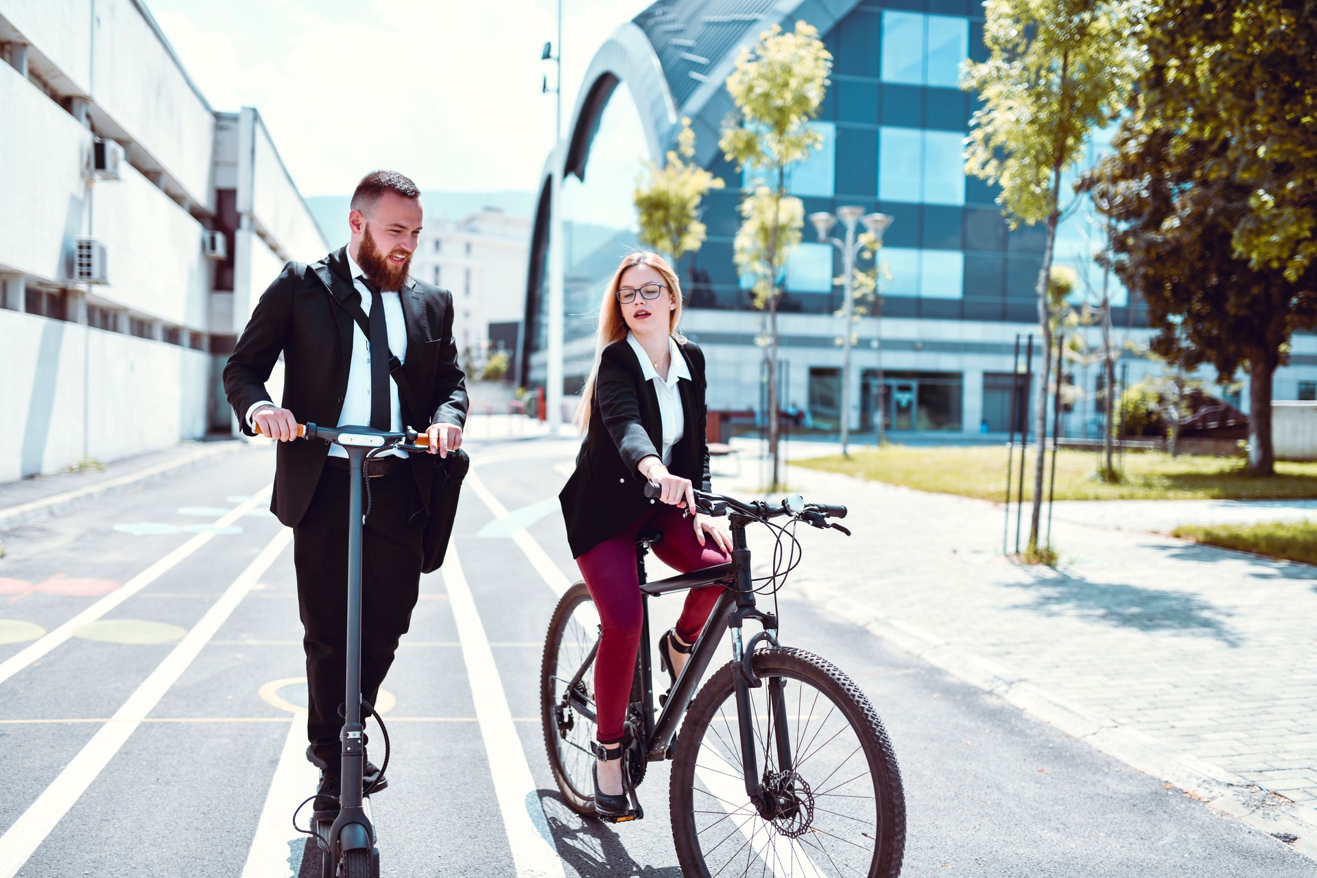 Elegantes Paar in Business-Kleidung Mit Spaß mit Fahrrad und Elektro-Scooter