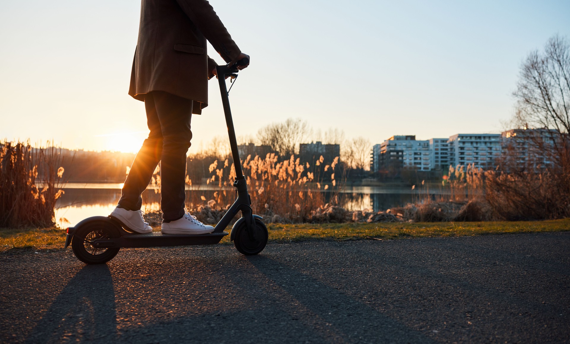 Unkenntlicher Mann, der bei Sonnenuntergang in der Stadt mit Elektroroller fährt