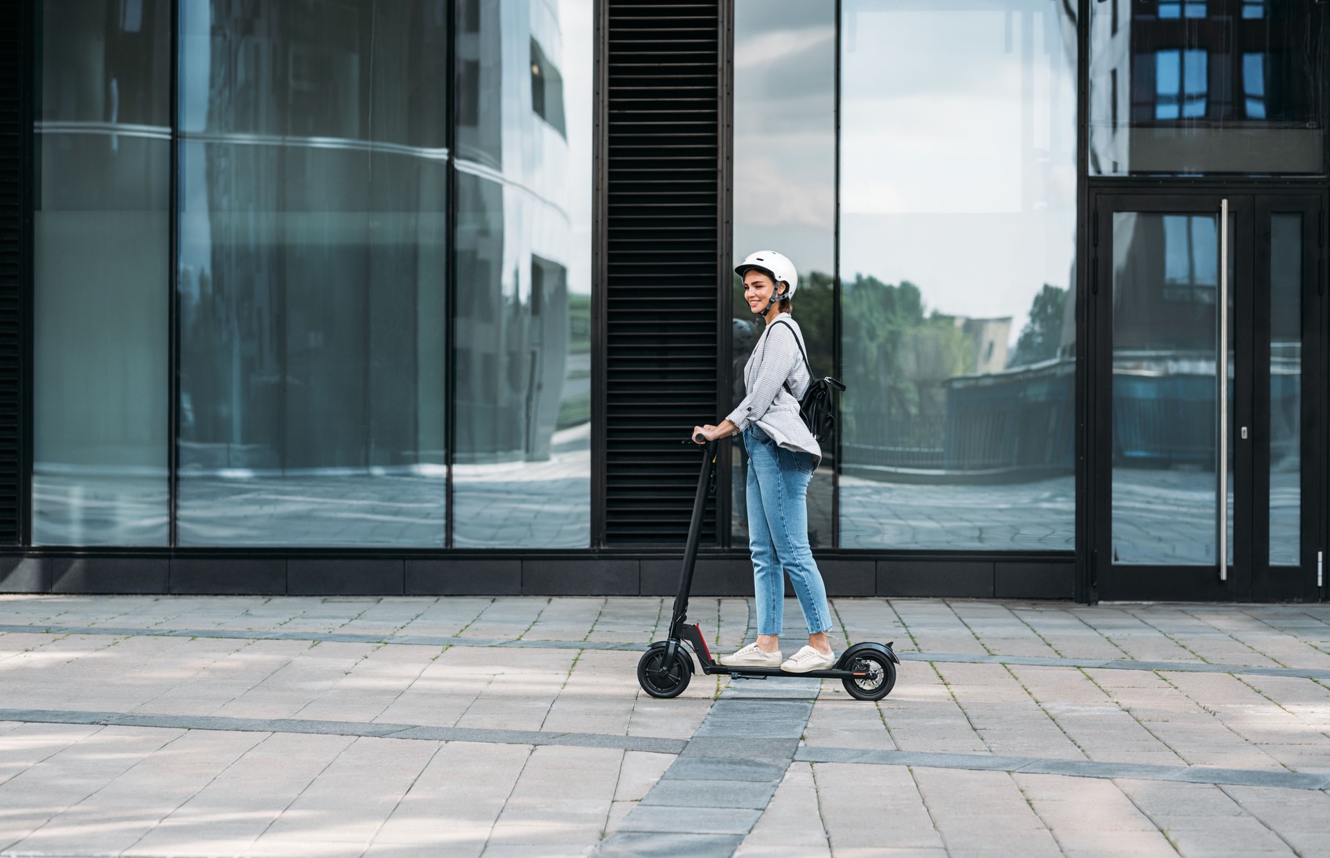 Junge Geschäftsfrau trägt Fahrradhelm fahren Push Scooter auf Fußweg